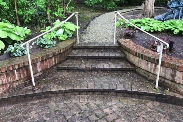 Brick steps with white metal railings lead up to a gravel path surrounded by greenery and plants, perfectly maintained by the top pressure washing service in Northeast Kentucky.