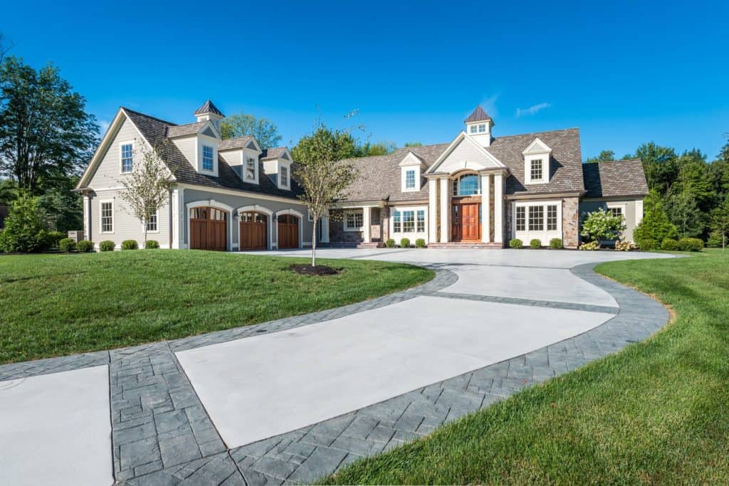 A large suburban home with a stone and wood facade, multiple gables, and a cupola gleams under the clear blue sky thanks to the best roof washing service in Northeast Kentucky. A curved driveway leads to wooden garage doors, bordered by a manicured lawn and trees.